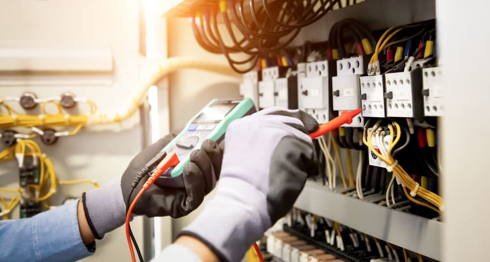 Electrician using a multimeter to test wires in a control panel for electrical diagnostics.